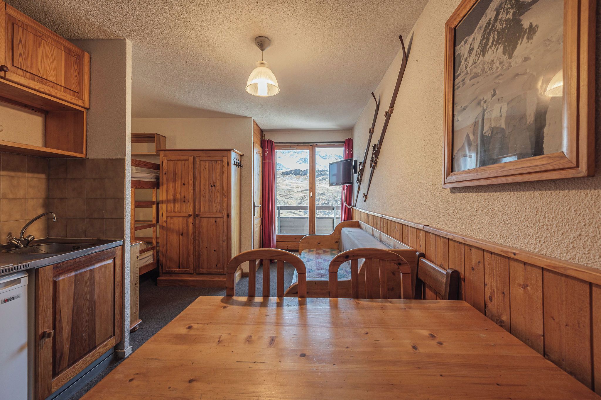 Ein Holzinterieur mit Esstisch, Stühlen, einer Küchenzeile und einem großen Fenster mit Blick auf eine verschneite Landschaft.