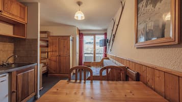 Ein Holzinterieur mit Esstisch, Stühlen, einer Küchenzeile und einem großen Fenster mit Blick auf eine verschneite Landschaft.