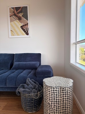Ein blaues Sofa, ein gemustertes Ottoman, ein Schachbrett und ein gerahmtes Bild an der Wand.