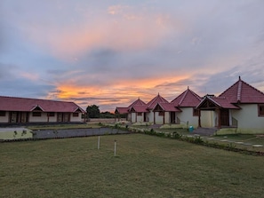 A row of traditional-style buildings with pitched roofs, a grassy foreground, and a sunset sky.