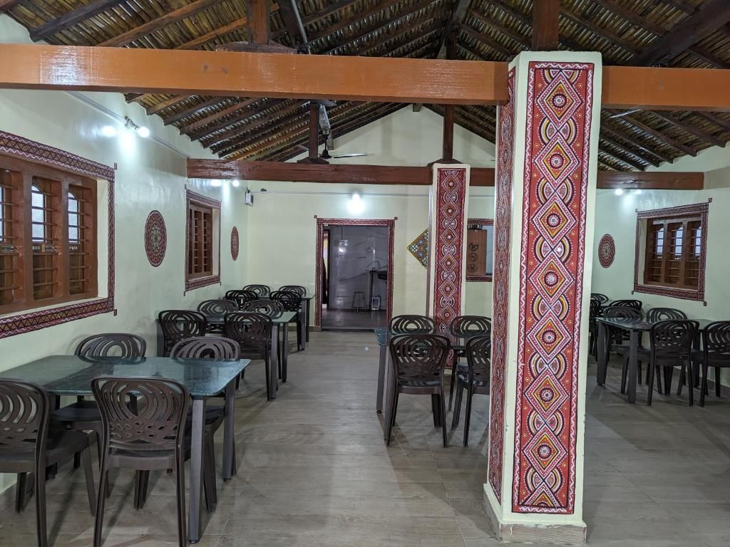 A dining area with multiple tables and chairs, a high ceiling with wooden beams, and patterned wall decorations.