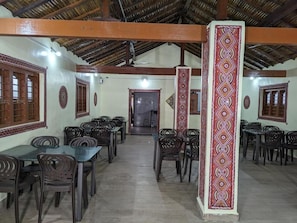 A dining area with multiple tables and chairs, a high ceiling with wooden beams, and patterned wall decorations.