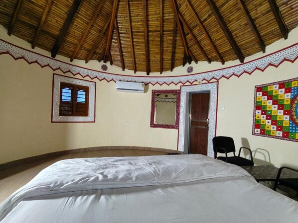 Una habitación con una cama, ventana, unidad de aire acondicionado, puerta y un colorido adorno de pared.