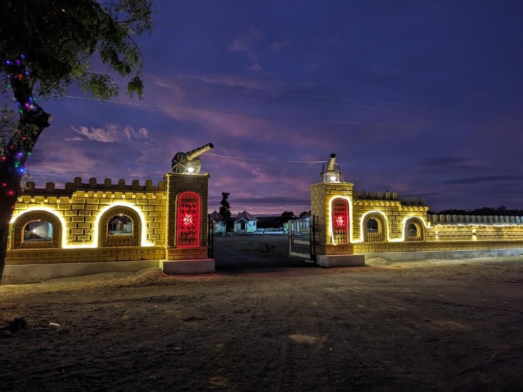 A brick gate with arched windows and a red door, illuminated by lights at dusk.