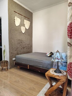 Een slaapkamer met een bed, nachtkastje, lamp, wanddecoratie en een potplant.