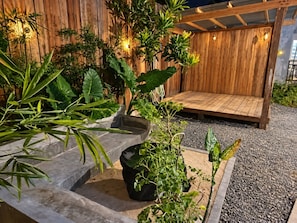 Een houten terras met een bankje, omringd door potplanten en een stenen plantenbak.