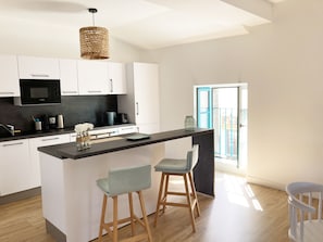 Une cuisine moderne avec des meubles blancs, un plan de travail noir et un luminaire suspendu.