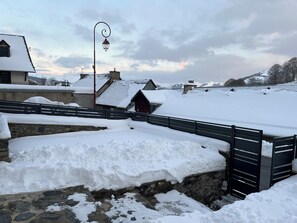Un paisaje nevado con un puente de piedra, una reja de metal y edificios con tejados cubiertos de nieve.