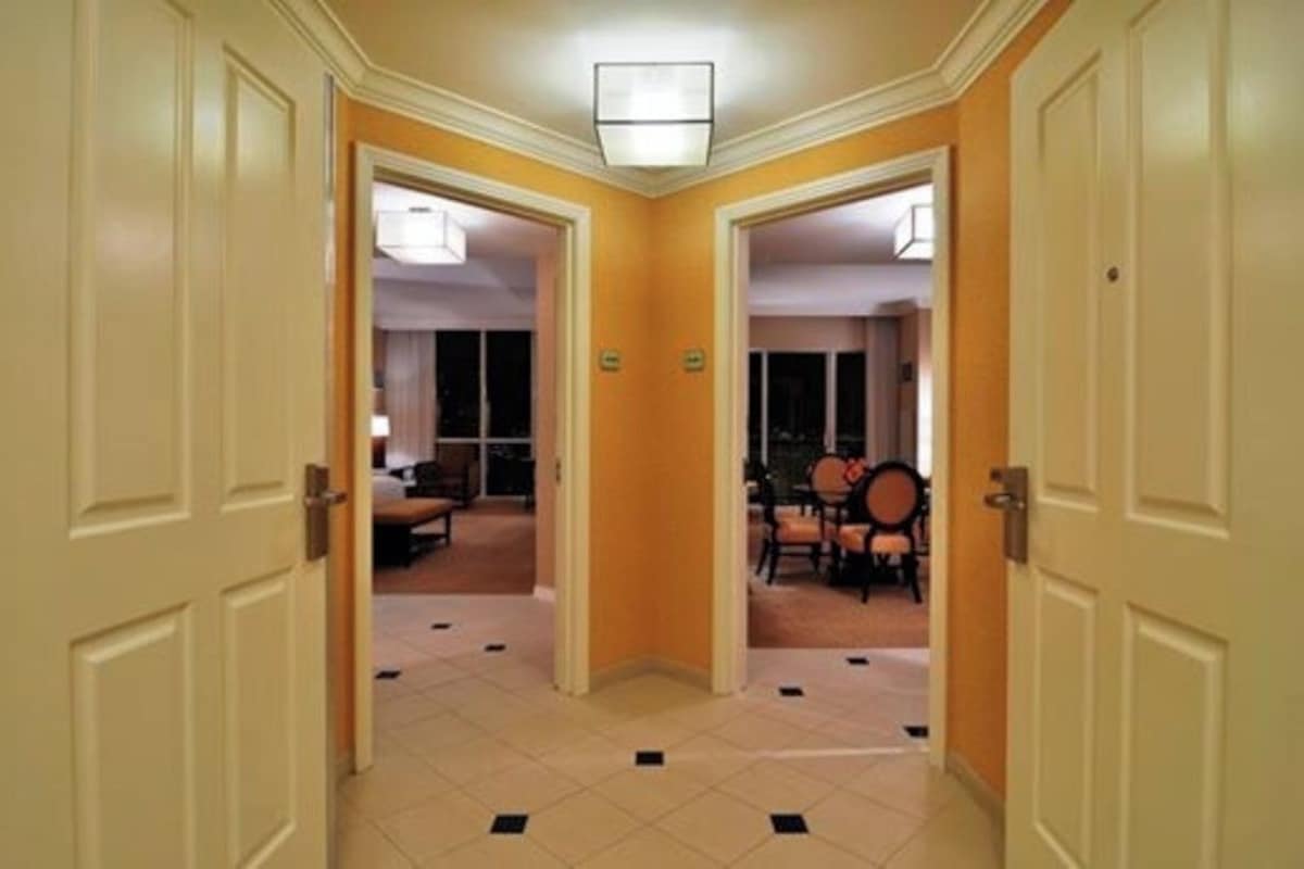 A hotel corridor with doors leading to rooms, a tiled floor, and a dining area with chairs and a table.