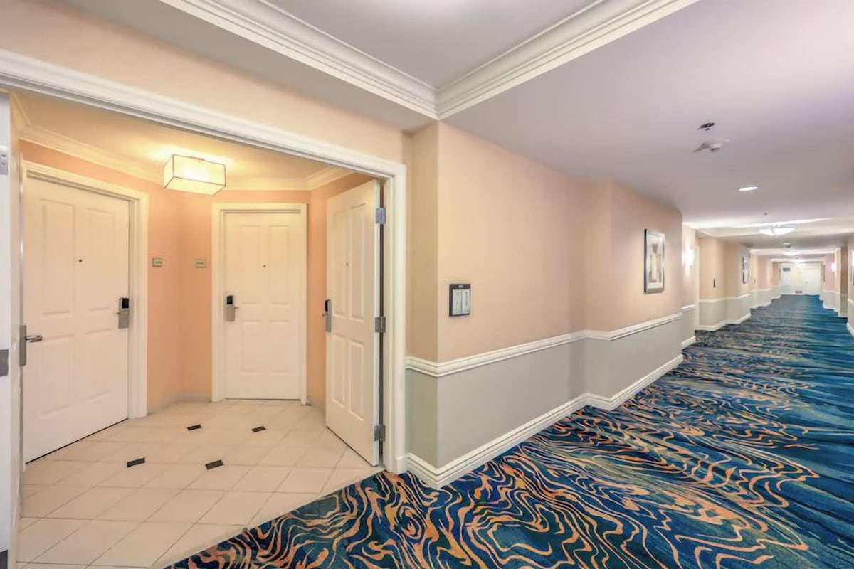 A hotel corridor with carpeted flooring, doors, and a light fixture.
