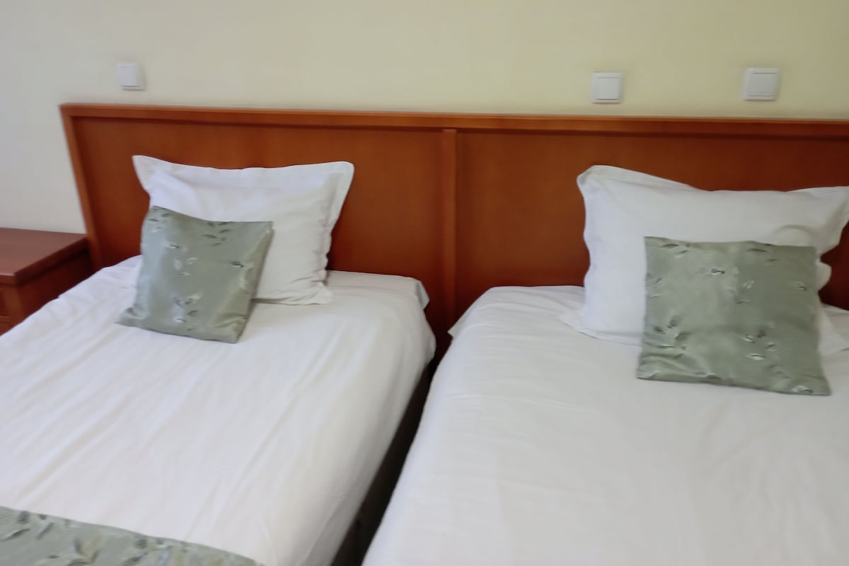 Dos camas individuales con cabeceros de madera y ropa de cama blanca, cada una con una almohada verde.