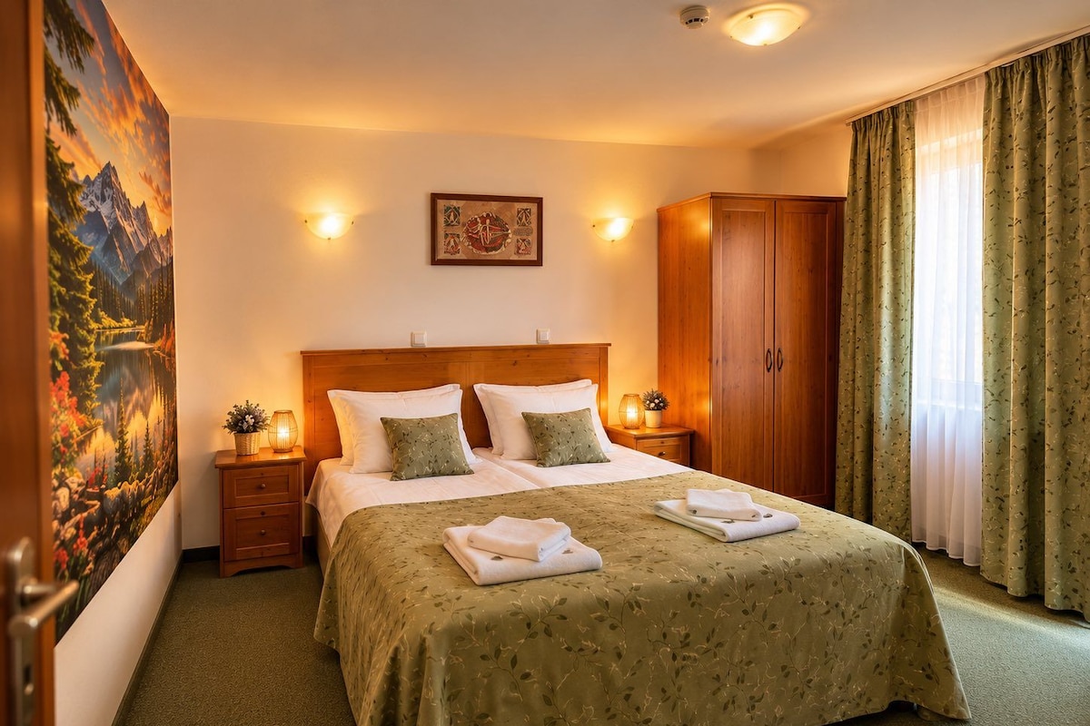 Habitación de hotel con una cama grande, dos mesitas de noche, un armario de madera, un cuadro en la pared y una ventana con cortinas.
