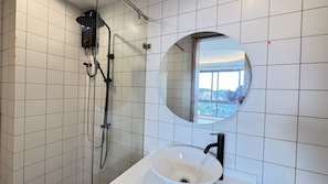 Een badkamer met een douche, een wastafel en een grote spiegel die uitzicht geeft op buiten.