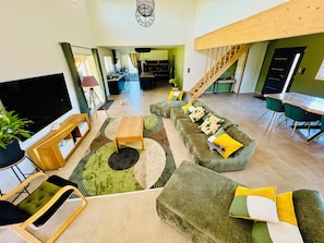 Amplia sala de estar con una televisión de pantalla plana grande, una mesa de centro de madera y un conjunto de sofás con cojines de colores.
