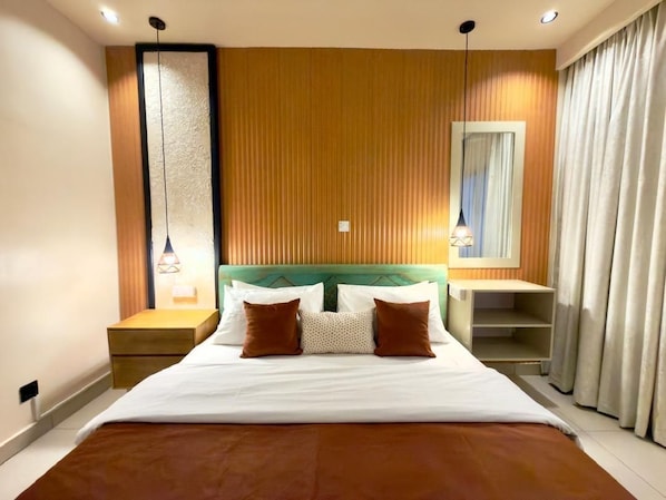 Habitación de hotel con una cama grande, pared de paneles de madera, lámparas de noche y un ventanal con cortinas.
