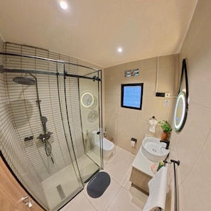 Un baño moderno con ducha envuelta en vidrio, un lavamanos, un espejo y un ventanal pequeño.