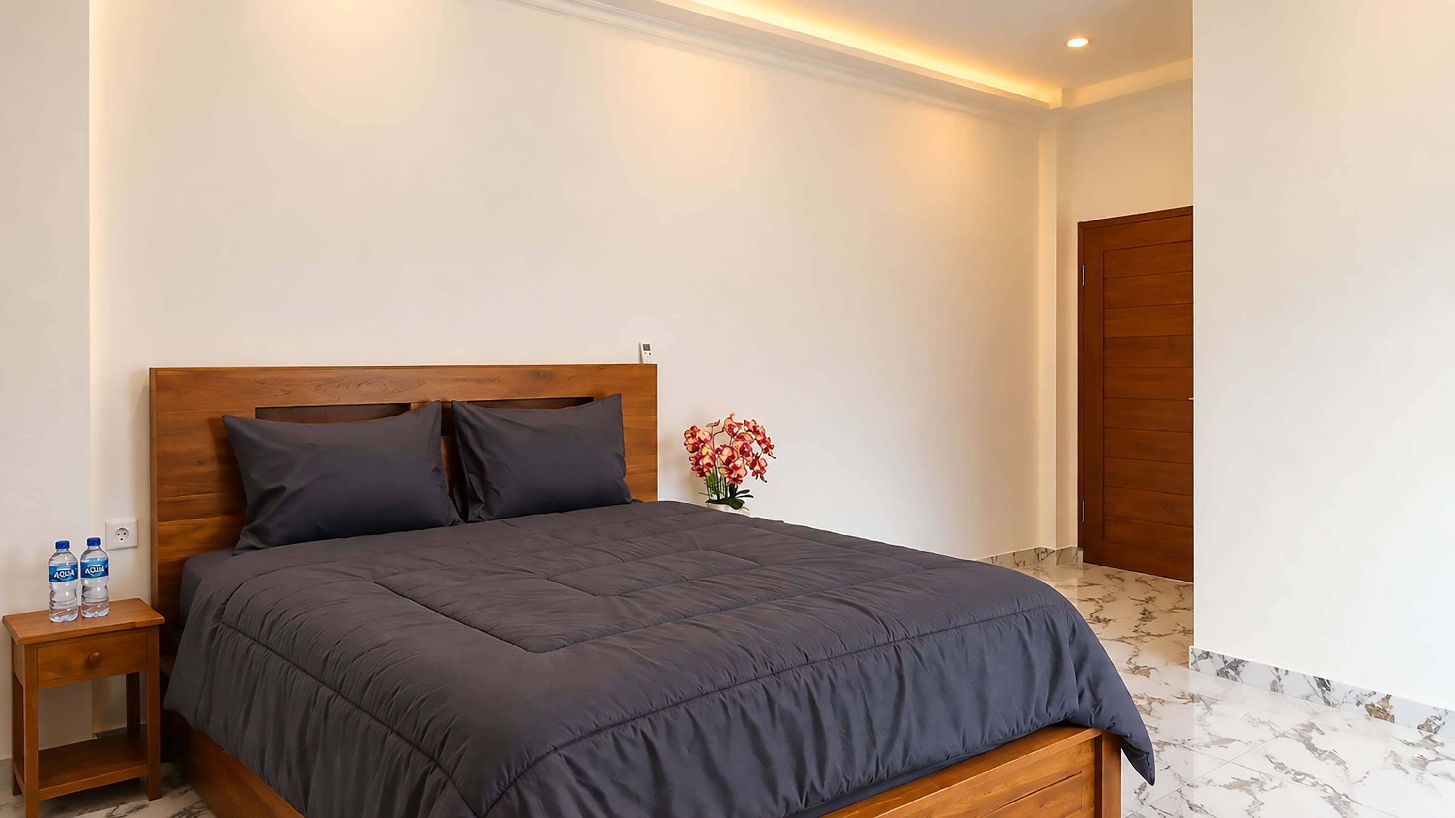 A bedroom with a bed, a nightstand, a vase with flowers, and a wooden door.