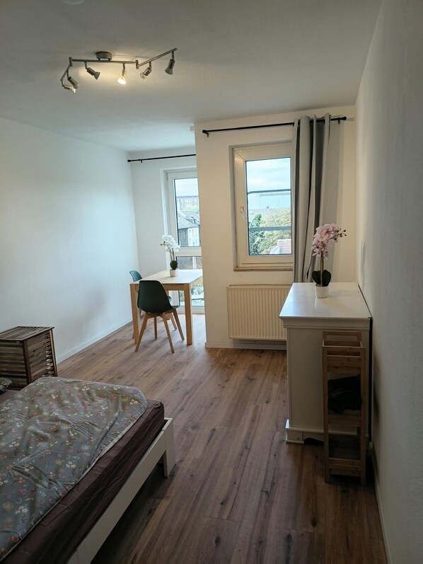 Ein Schlafzimmer mit einem Bett, einem Schreibtisch, einem Stuhl, einem Heizkörper und einem Fenster mit Vorhängen.