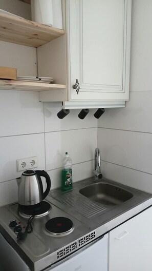 Eine Küchenzeile mit einem Edelstahl-Wasserkocher, einer Flasche Spülmittel, einem Waschbecken und einem Schrank darüber.