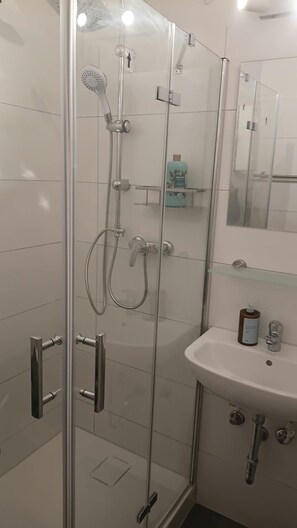 Ein modernes Badezimmer mit einer begehbaren Glasdusche, einem weißen Waschbecken und einem Spiegel darüber.