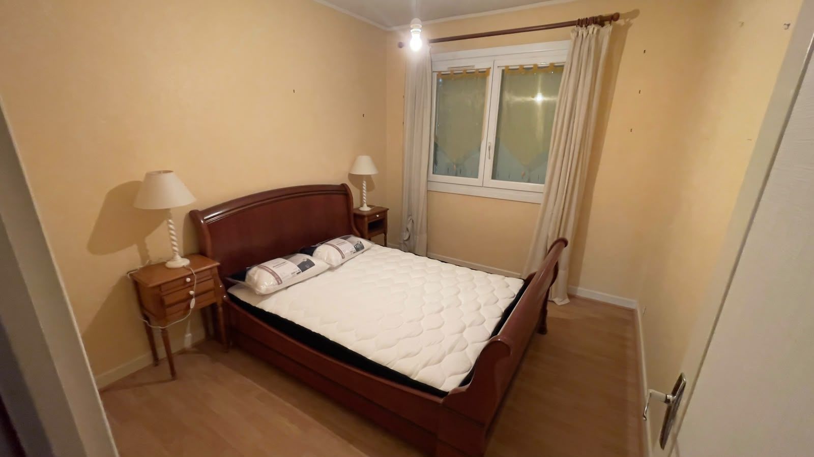 Un dormitorio con cama de madera, mesitas de noche, una ventana con cortinas y una lámpara.