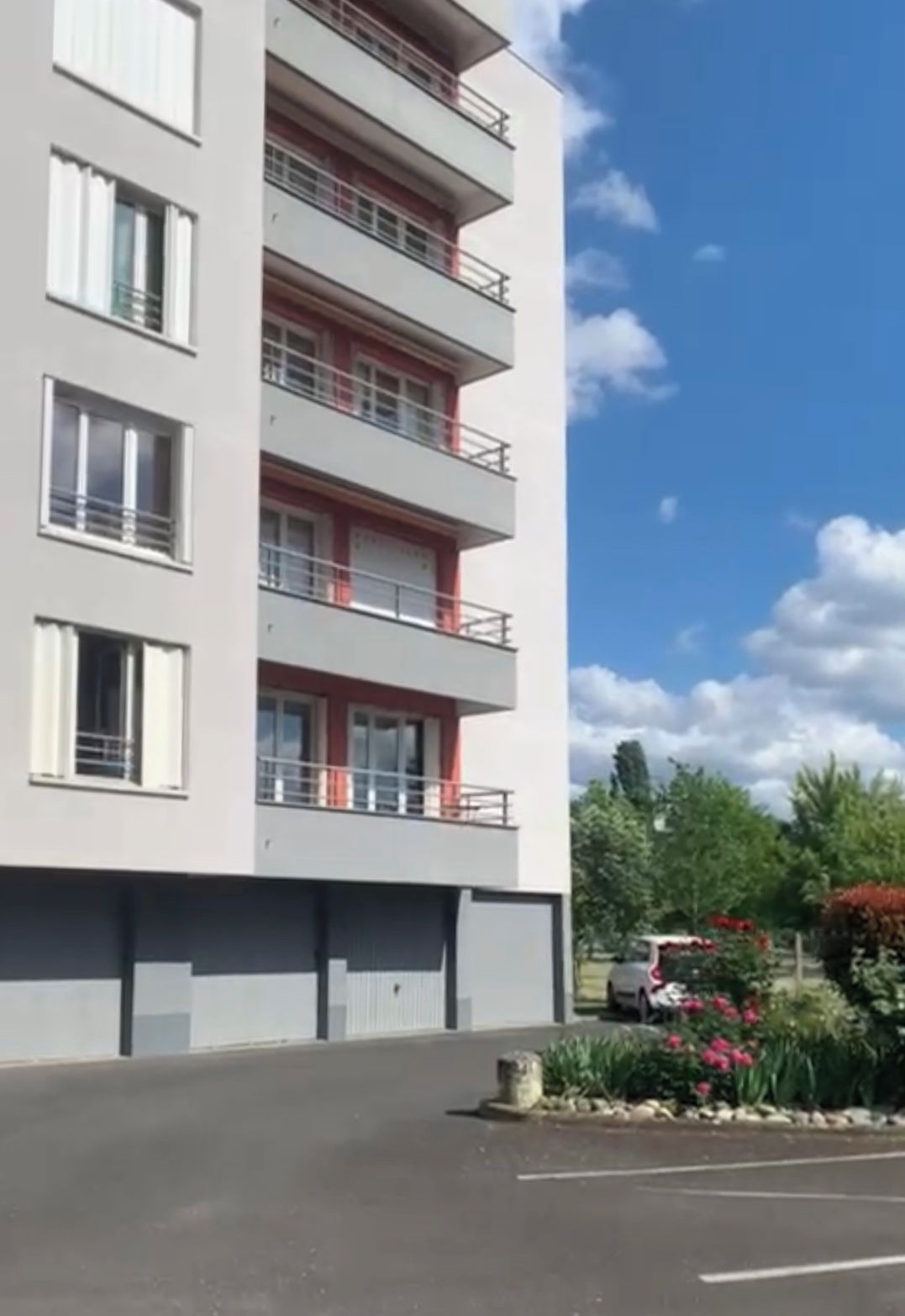Un edificio residencial de varios pisos con balcones y un estacionamiento al frente.
