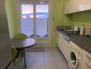 Cozinha compacta com máquina de lavar roupa, mesa de jantar com cadeiras e vista pela janela.