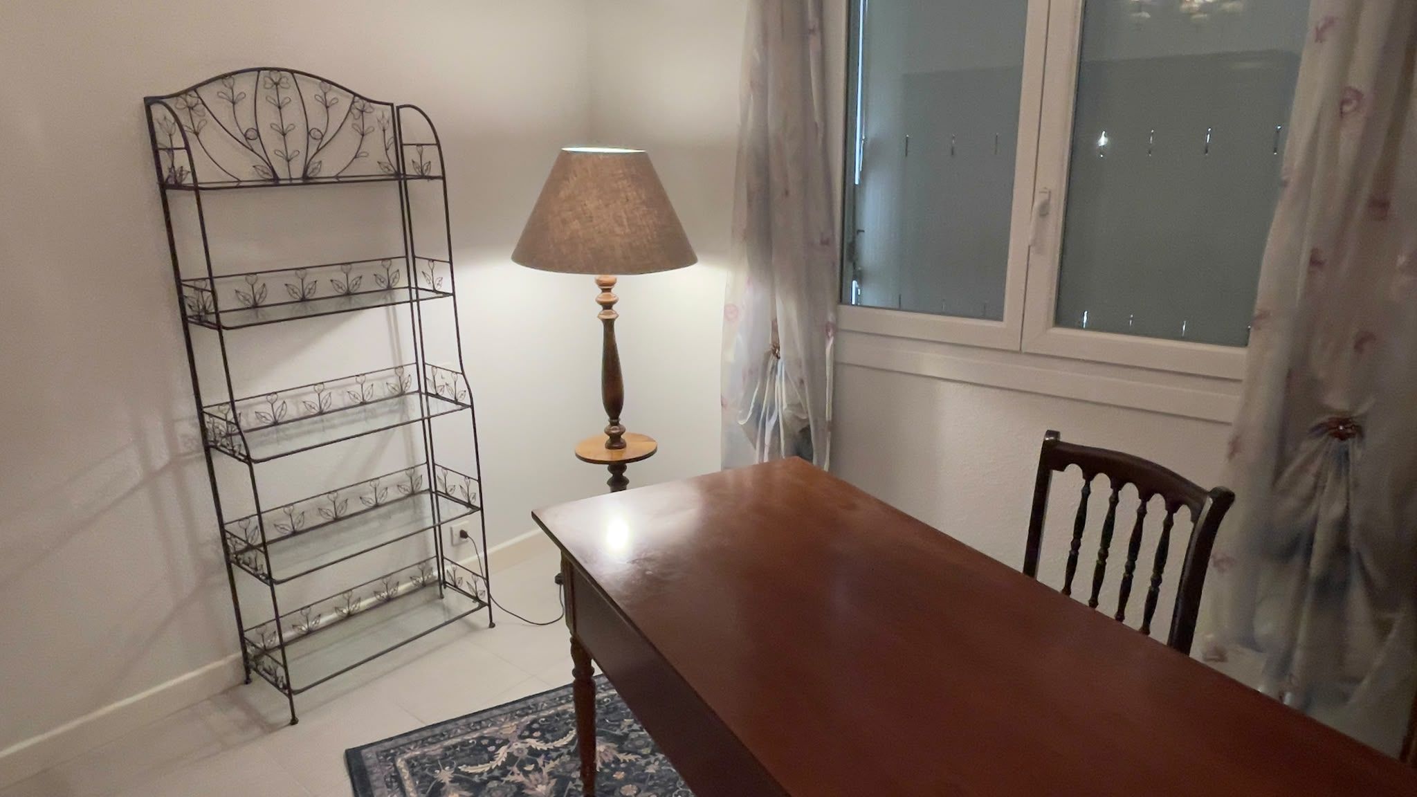Un comedor con mesa de madera, una silla, una lámpara y una estantería metálica en la pared.