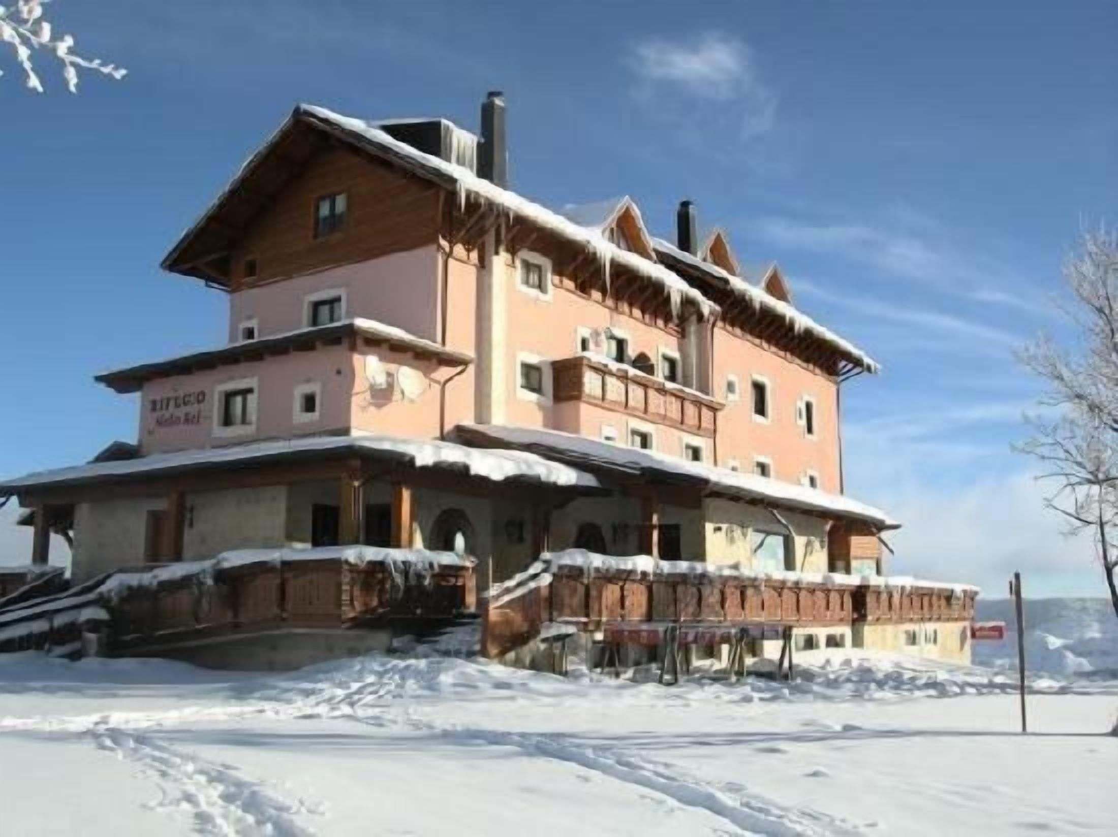 Un edificio de varios pisos con techo inclinado, probablemente un hotel o refugio, con fachada cubierta de nieve y cielo despejado.