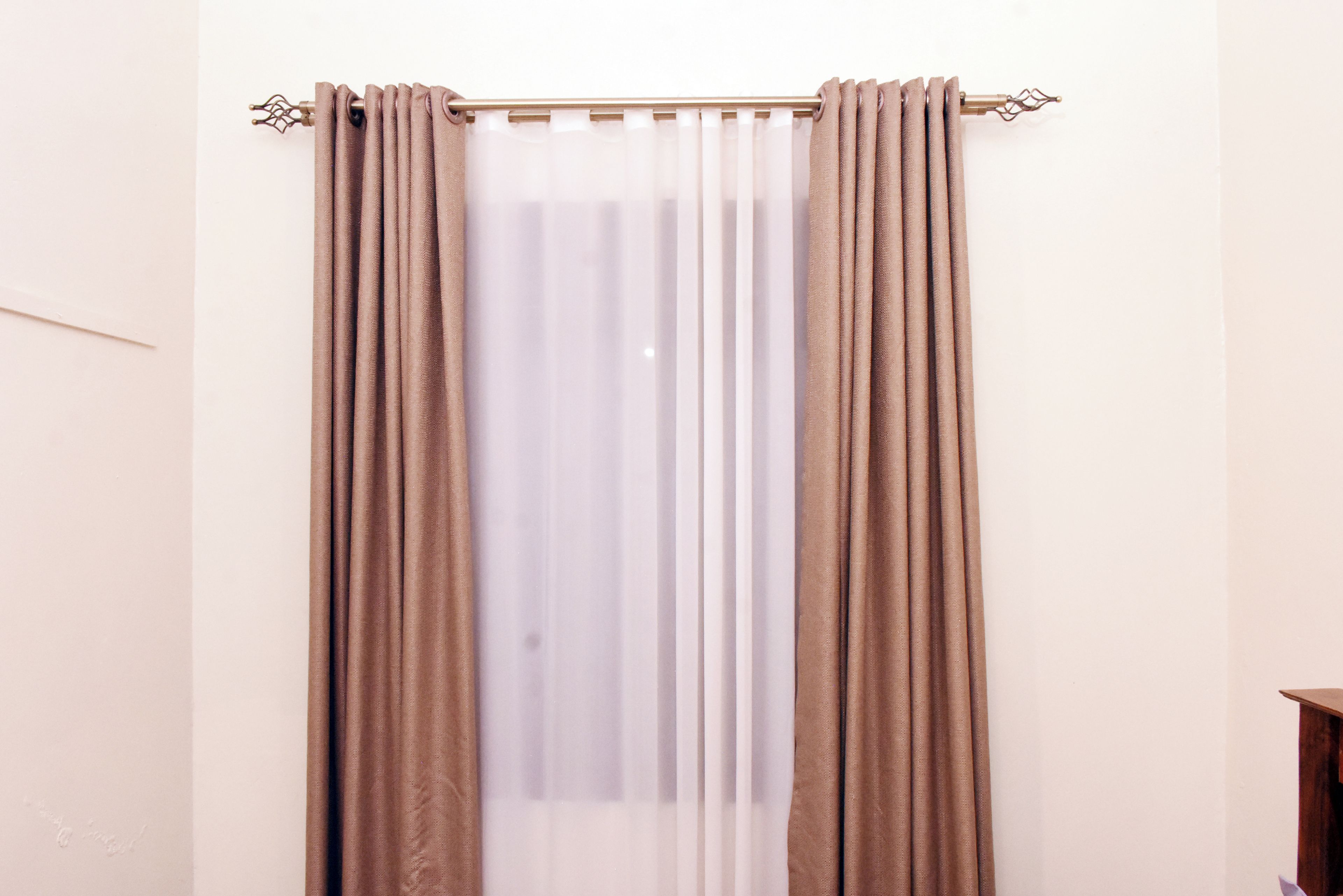 A room with a window covered by beige curtains and a curtain rod.