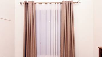A room with a window covered by beige curtains and a curtain rod.