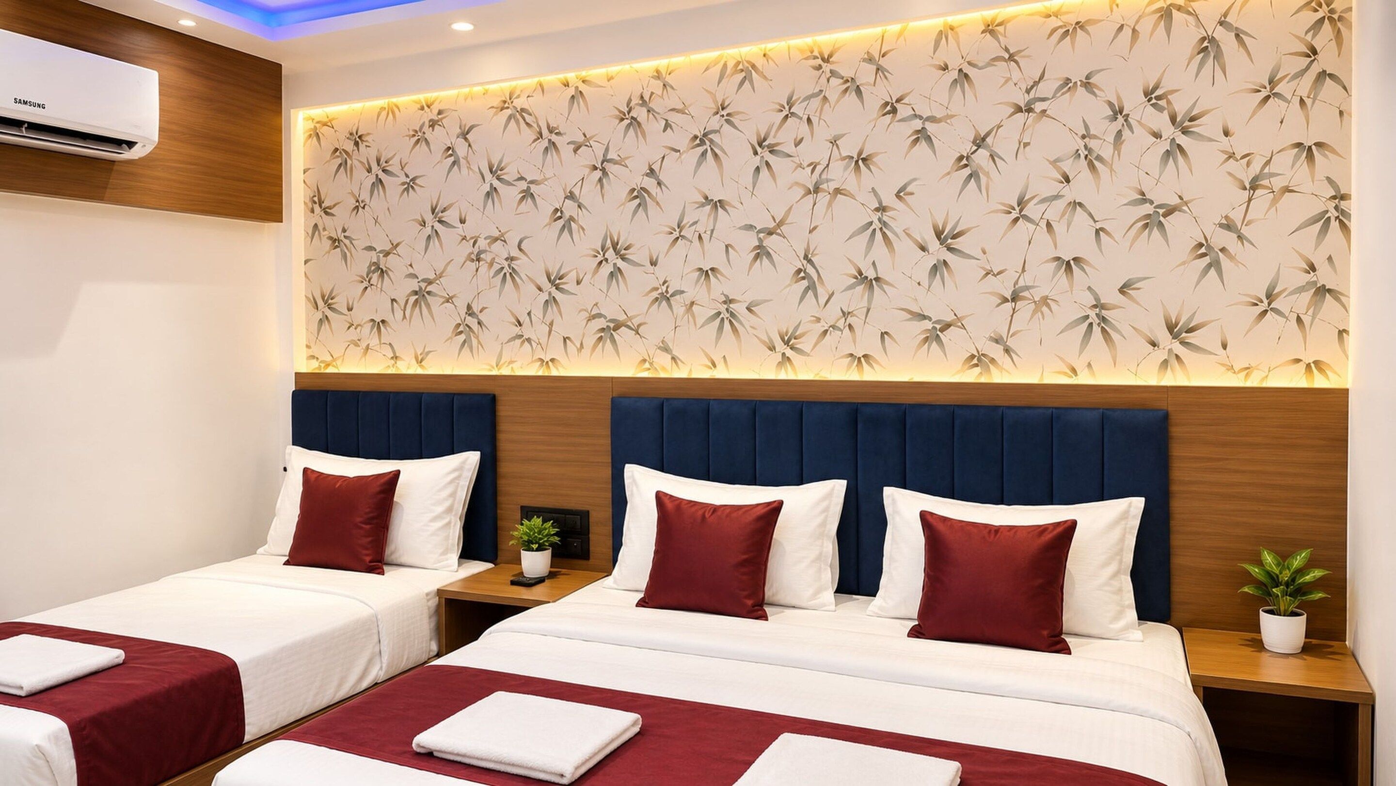 A hotel room with two beds, a wall-mounted air conditioner, a bamboo leaf wallpaper, and a nightstand with a plant.