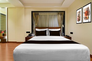 A hotel room with a large bed, a nightstand, a bedside table, and a wall with two framed pictures. - Deluxe Room Alamin International (Kolkata)