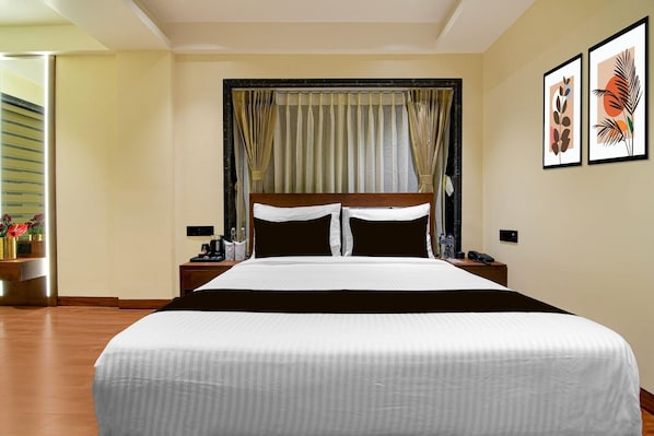 A hotel room with a large bed, a nightstand, a bedside table, and a wall with two framed pictures. - Deluxe Room Alamin International (Kolkata)