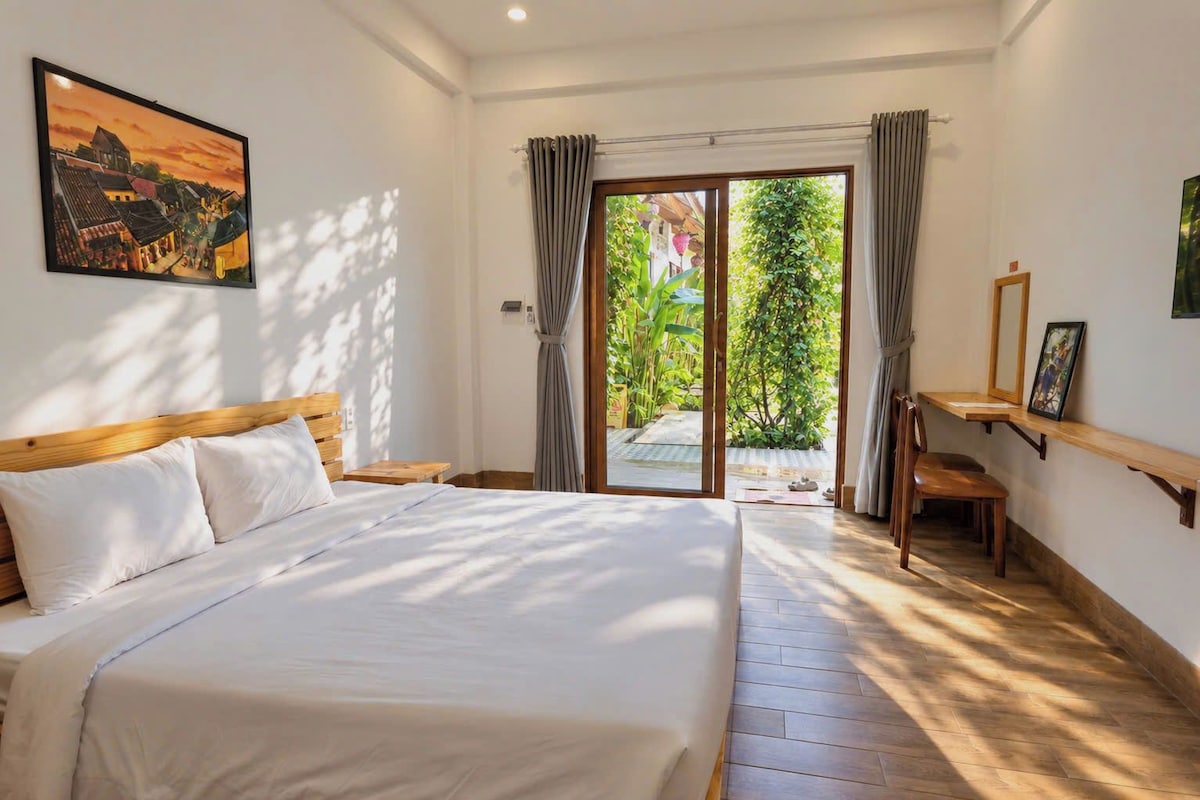 Ein Schlafzimmer mit einem großen Bett, einem Schreibtisch und Blick auf einen Garten durch eine Schiebetür.