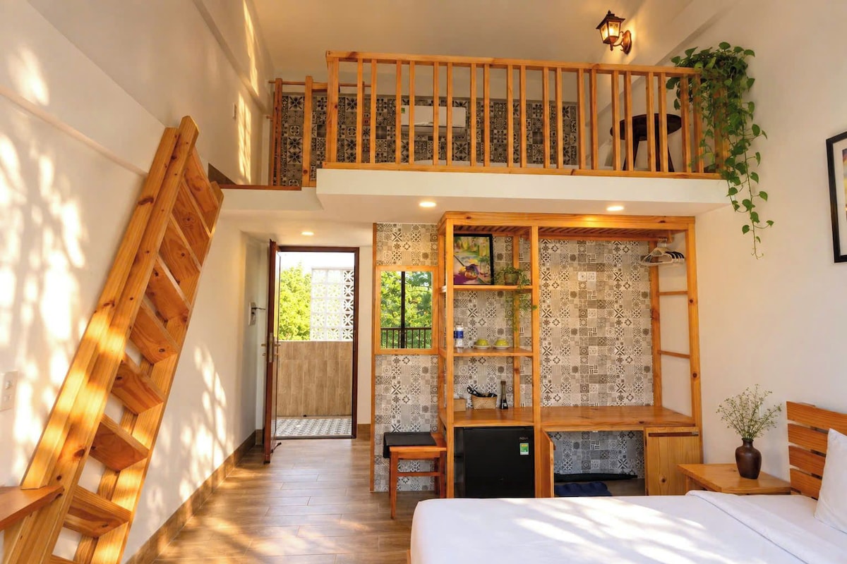 Ein Schlafzimmer mit einer erhöhten Schlafkoje, einer Holzleiter, einem Bett, einem Schreibtisch und einem kleinen Kühlschrank.