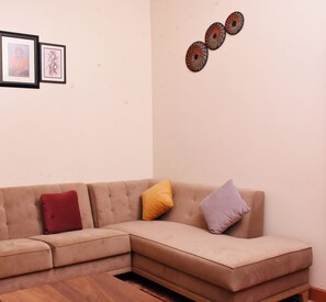 Un divano modulare beige con tre cuscini rossi, gialli e viola, un tavolino in legno e tre decorazioni circolari appese al muro.