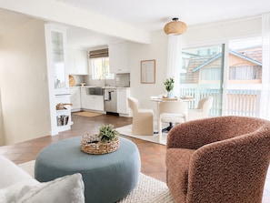 Een moderne woonkamer met een keuken op de achtergrond, een eethoek met twee stoelen, en een balkon met uitzicht.