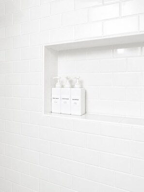 A bathroom with white tiled walls and a shelf holding three white bottles labeled body wash, conditioner, and shampoo. - Steps to the Beach, Quiet, New, Intuit, Crypto, Sofi, LAX, Venice, Santa Monica (Manhattan Beach)