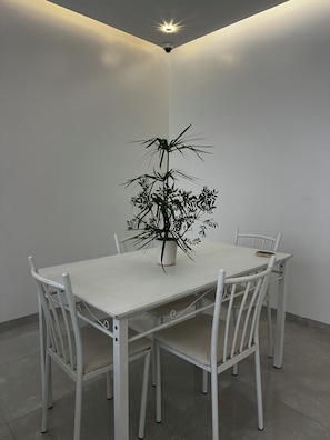A white dining table with four chairs, a potted plant, and a ceiling-mounted security camera. - Dar Lalla Yasmina Guesthouse 5-bedroom bed with private bathroom in  Tangier (Tanger)