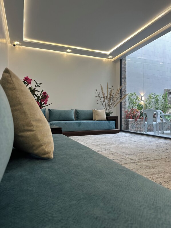 A modern living room with a sofa, cushions, and a view of a garden through large windows. - Dar Lalla Yasmina Guesthouse 5-bedroom bed with private bathroom in  Tangier (Tanger)