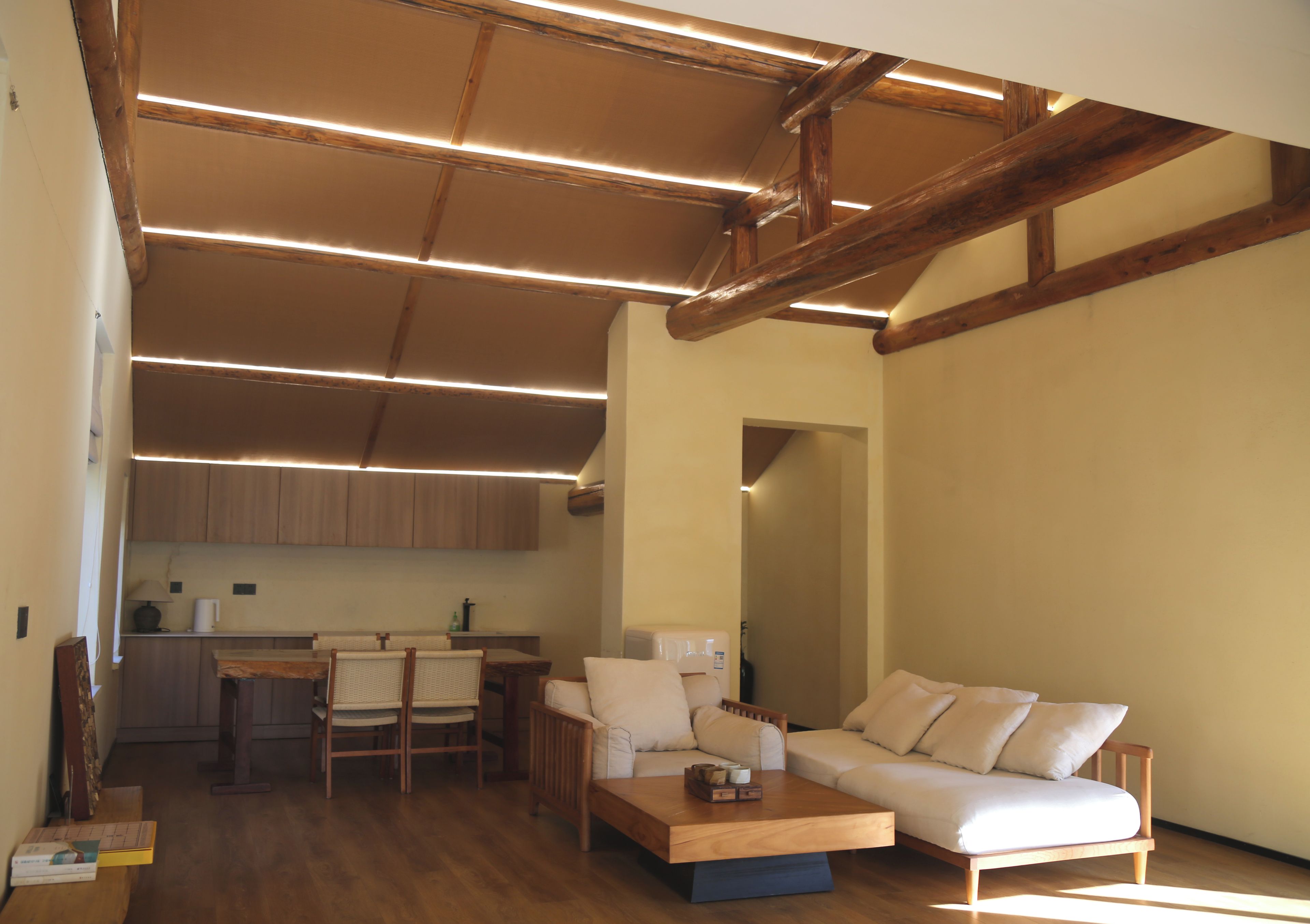 Amplia sala de estar con techo de madera, un sofá, una mesa de centro y una cocina al fondo.