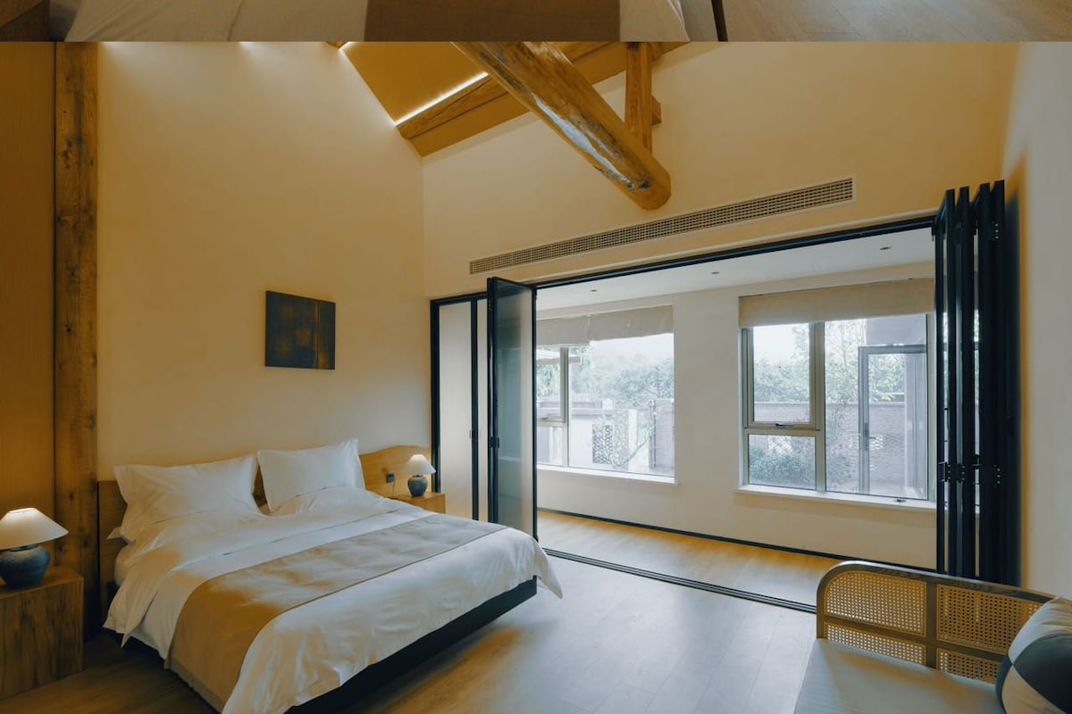 A hotel room with a bed, a small table, chairs, and a view of the outdoors.