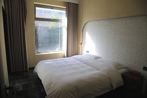 Quarto de hotel com cama, janela com cortinas e cabeceira com padrão de tijolos.