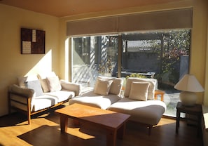 Sala de estar iluminada pelo sol, com um sofá, uma mesa de centro de madeira e um abajur.