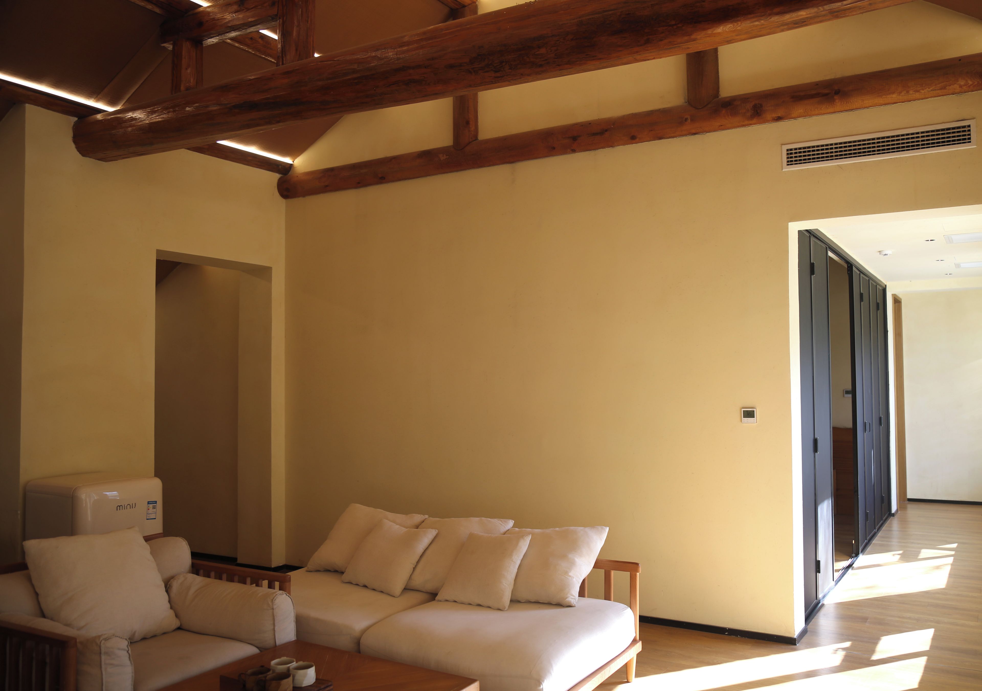 Una habitación con sofá, una mesa con tazas, vigas de madera en el techo y una puerta que da a otra estancia.