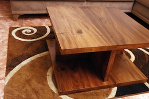 Un tavolo in legno con piano quadrato e ripiano inferiore, posizionato su un tappeto decorato.