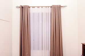 Une pièce avec une fenêtre recouverte de rideaux beiges et une tringle à rideaux.