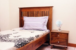 Un letto singolo con una testiera in legno, un comodino con una ventola e una coperta a motivi.