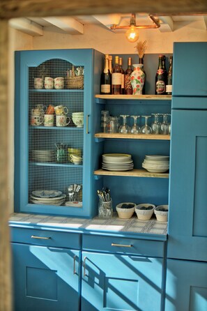 A kitchen with blue cabinets, a wire mesh cabinet, and shelves with dishes and bottles. - New Listing (Saint-Philbert-des-Champs)